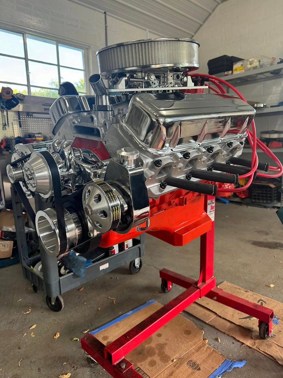 Fully restored classic car engine with chrome components and red wiring, mounted on an engine stand in a workshop.