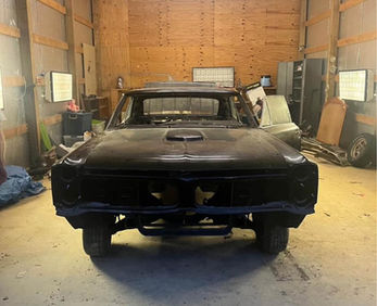 Classic car undergoing restoration in a workshop, black body stripped down, ready for repair.
