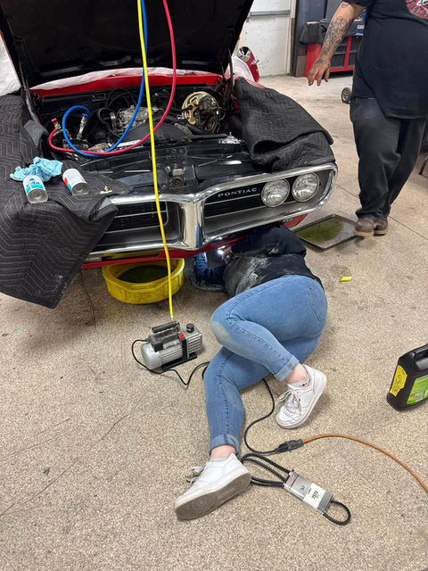 Classic car restoration in progress, mechanic working on a red Pontiac GTO engine in a garage. 