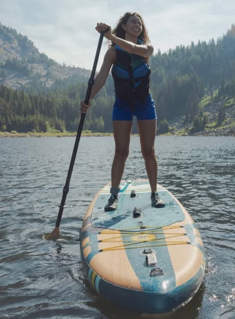 A woman paddleboarding on a calm lake with a paddle.