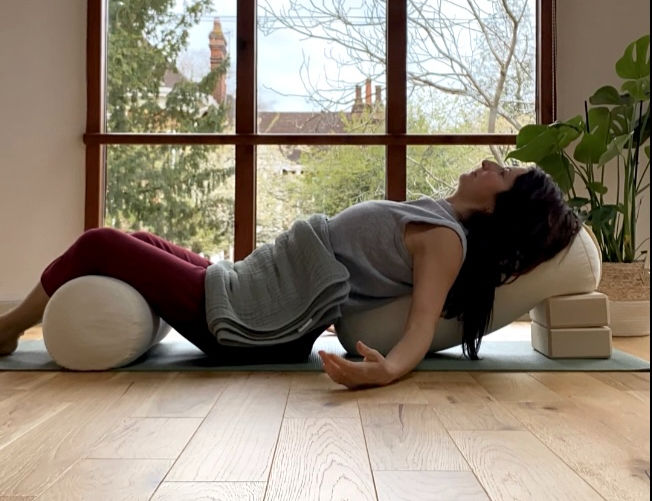 a lady in a reclined relaxing yoga yin position with blocks and bolster as props to support her body