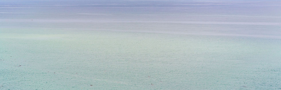 Calm, light turquoise sea stretching to the horizon under a soft, cloudy sky. No visible objects or text. Serene and peaceful mood.