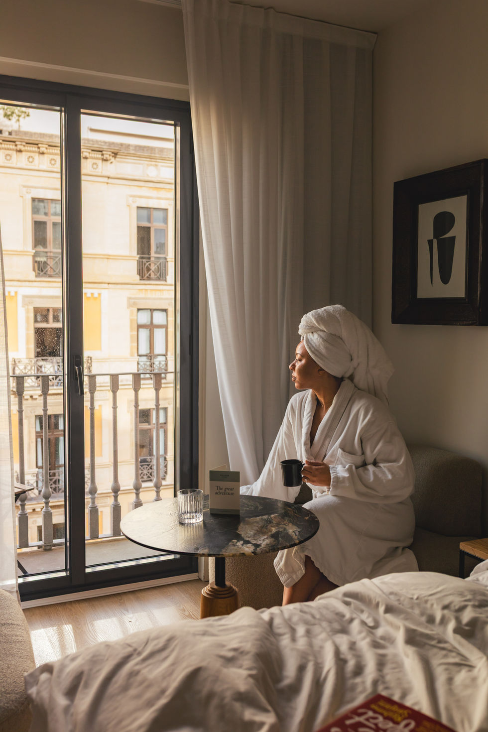 black woman in robe looking out the window 