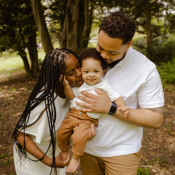 Black family of three. Mom and dad holding son in the park.