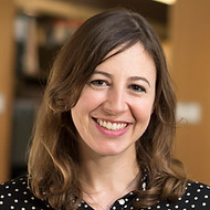 Gina is a white woman with medium length brown hair. She is wearing a black and white polkadot shirt. Her smile is big and welcoming.