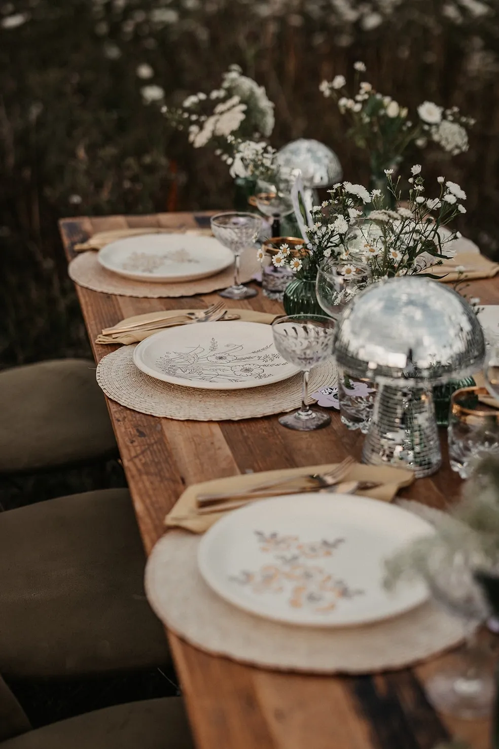 A rustic wedding breakfast table, using white floral plates and neutral colors. Gold cutlery and green foliage. Supplied and decorated by Disco Dining, an LGBTQ+ wedding supplier part of the Rebel Love Directory
