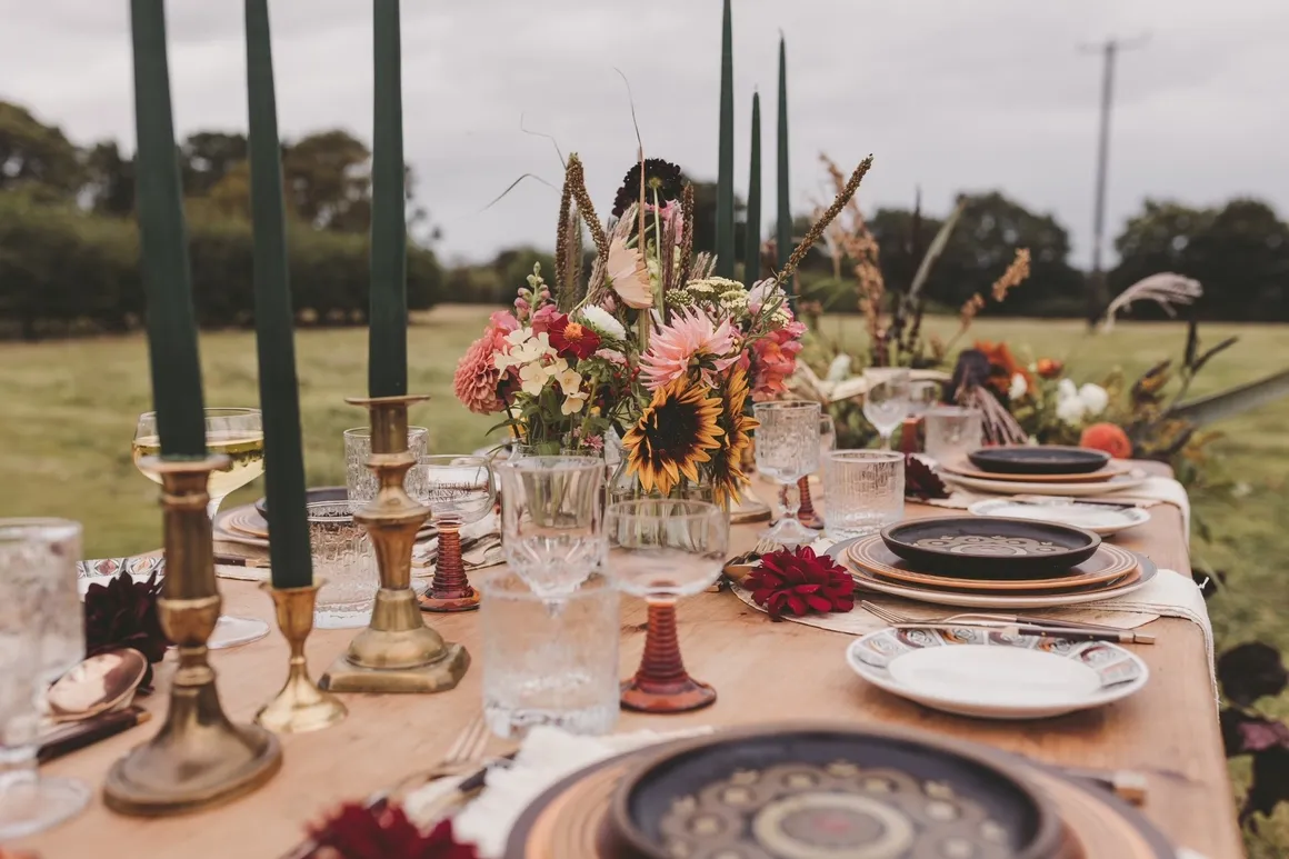 Wedding breakfast table decoration, including gold candlestick holders and green candles, aswell as plates, glasses and flowers. Supplied and decorated by Disco Dining, an LGBTQ+ wedding supplier part of the Rebel Love Directory