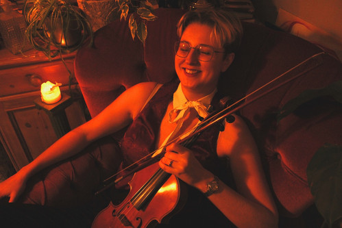 Photo of Shane in low, red lighting, holding a violin. Shane Considine is an LGBTQ+ musician offering baroque and classical music for weddings, part of the Rebel Love Directory.