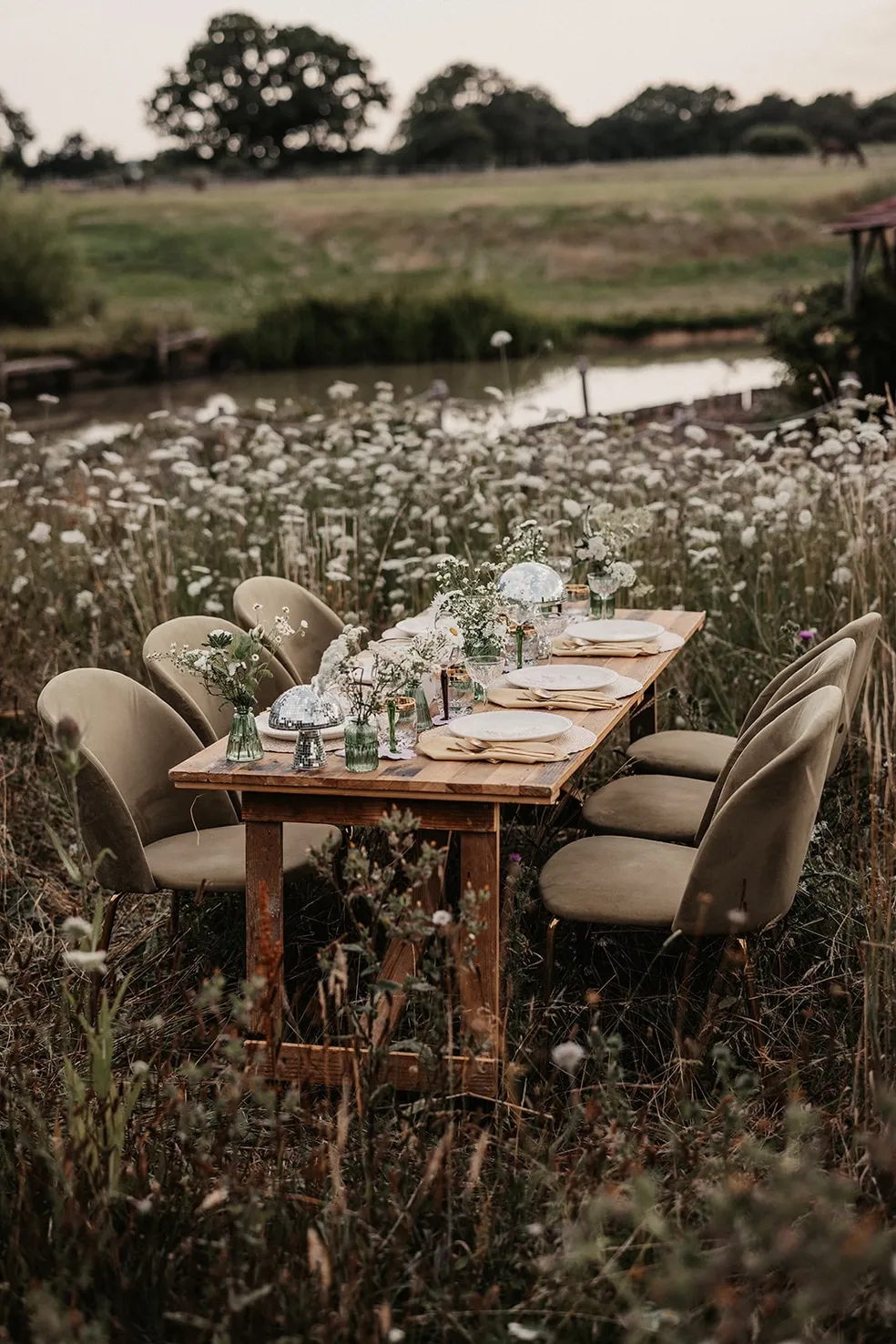 Wedding table decoration, set outdoors in a bed of flowers. Using a wooden rustic table and chairs and decorated with flowers. Supplied and decorated by Disco Dining, an LGBTQ+ wedding supplier part of the Rebel Love Directory