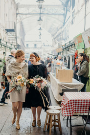 LGBTQ+ newly-weds walk through St Nicholas' Market in Bristol wedding florals by Lucy Coco Florist, part of LGBTQ+ inclusive suppliers directory, Rebel Love Directory