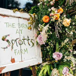 The Barn at Sprotts Farrm wooden sign amongst pink, white and green florals