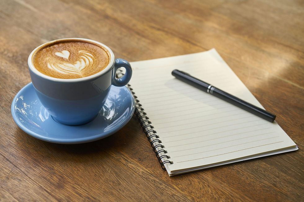 coffee in blue mug and saucer next to a notebook and pen on a wood backdrop