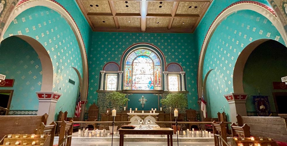Church altar with a stained glass window over a silver crucifix; candles surround the altar