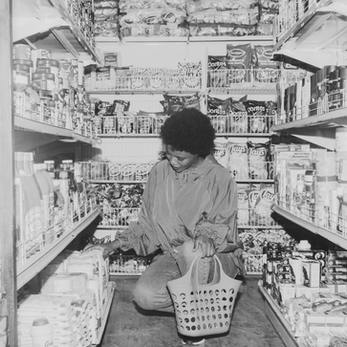 Woman kneeling on the floor of a grocery store, selecting items from a lower shelf
