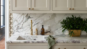 Integrated marble sink with vein-matched countertop and backsplash, brass faucet, and neutral cabinetry.