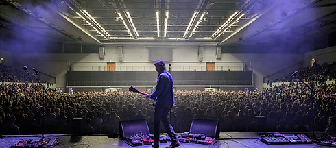 Musician performing on stage in front of packed indoor venue, highlighting professional live sound system integration