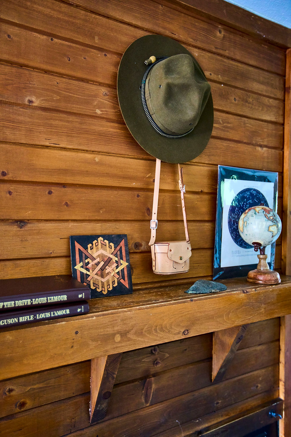 Hat and art decor on wooden shelf in rustic cabin decor.
