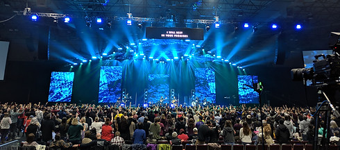 Congregation at worship event with stage lighting and AV displays, demonstrating reliable installed audio visual systems