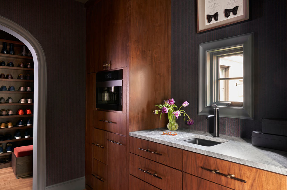 A spacious, organized closet with built-in shelves, glass shelving, and polished brass handles.