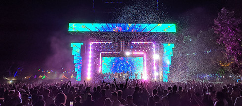Outdoor music festival crowd in front of a colorful LED-lit AV stage, showcasing large-scale live event audio visual systems