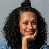Aisha Fletcher rests her chin on her hand, dark curly hair, portrait photo.