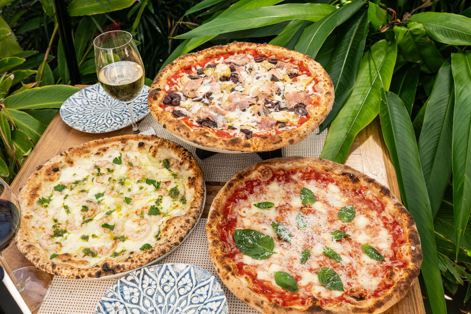 Three pizzas, white wine, and plates on an outdoor table