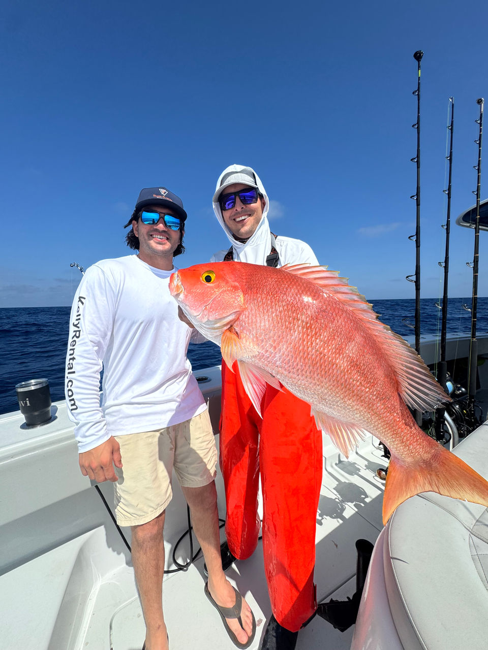 Two men on a boat holding a large red fish