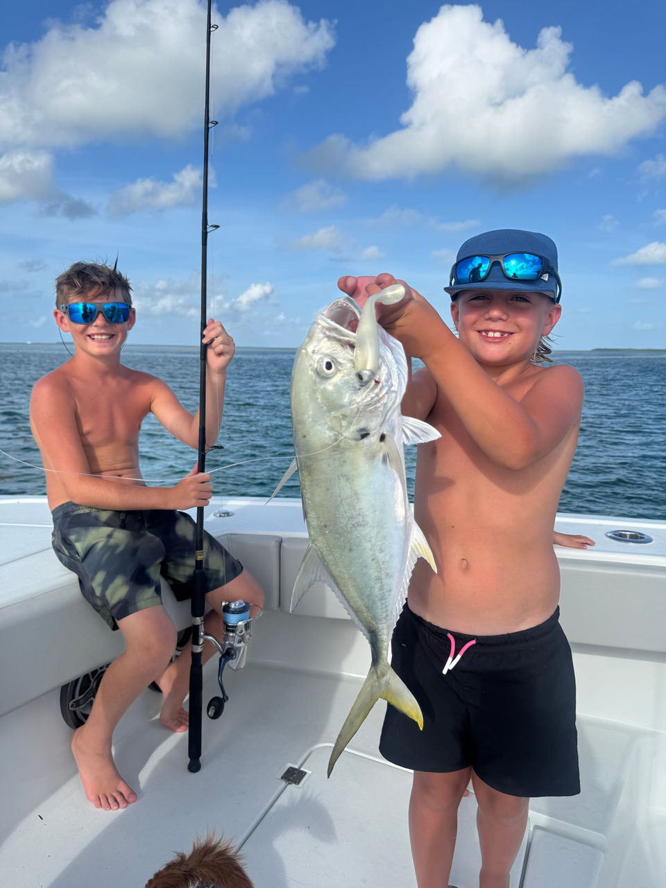 Two boys on a boat, one holding a large fish, the other with a fishing rod