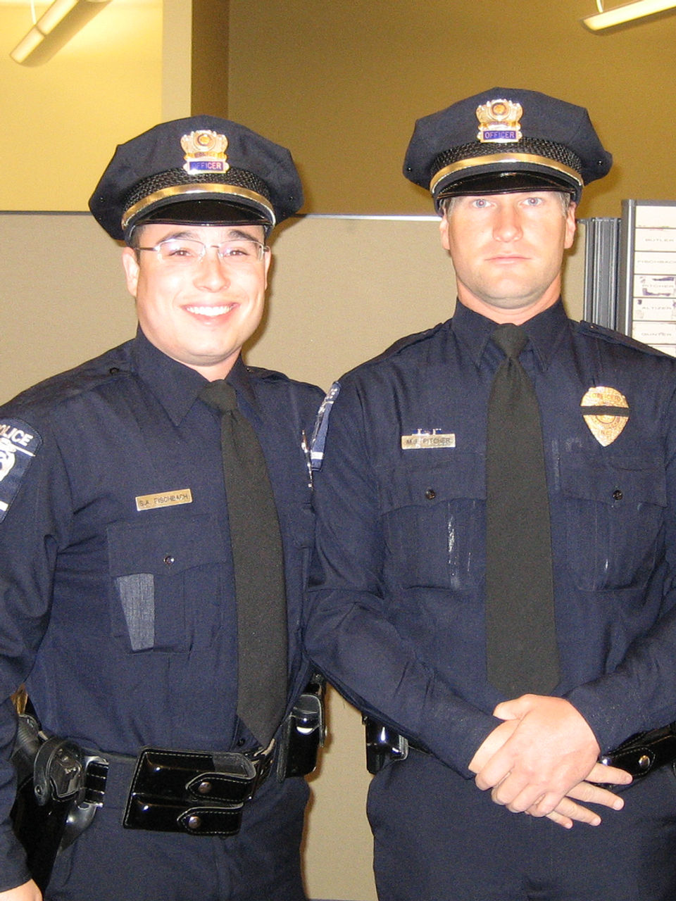 Two uniformed police officers smiling and posing with a dark background.