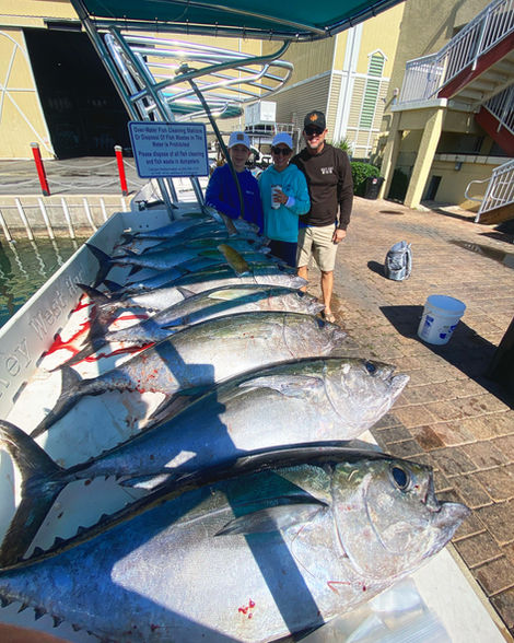 Three people proudly display their large fish catch on a boat deck