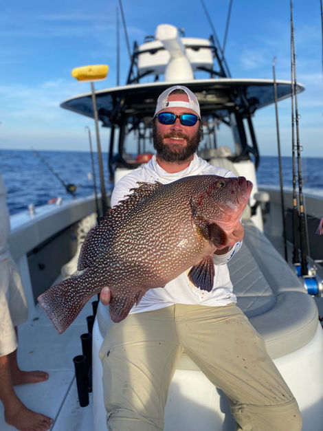 Smiling man holding a large spotted fish on a fishing boat