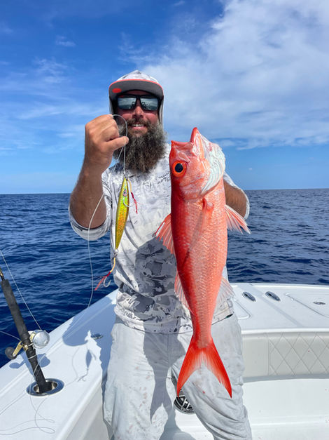 Bearded man holding a red snapper on a boat