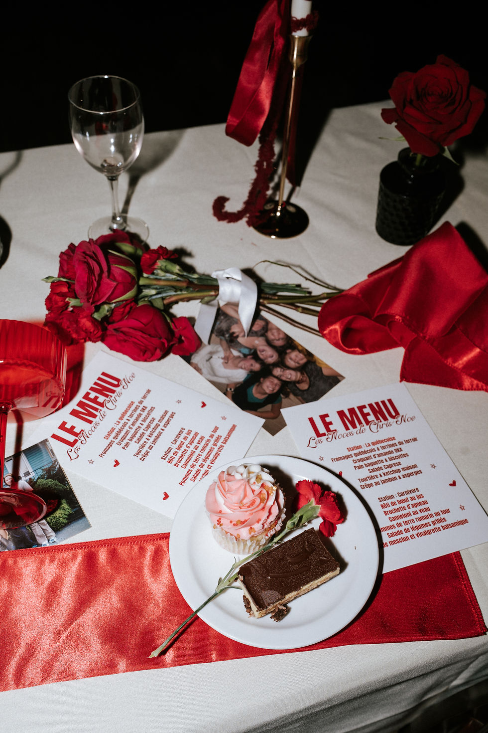 Table de fête avec menus, roses rouges et pâtisseries.