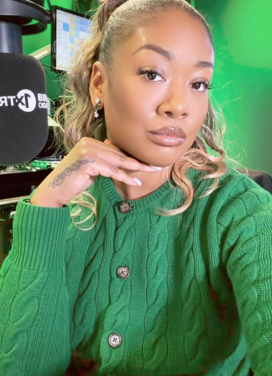 Sian Anderson in a green sweater poses with hand under chin in a radio studio. Black microphone visible, green background, calm expression.