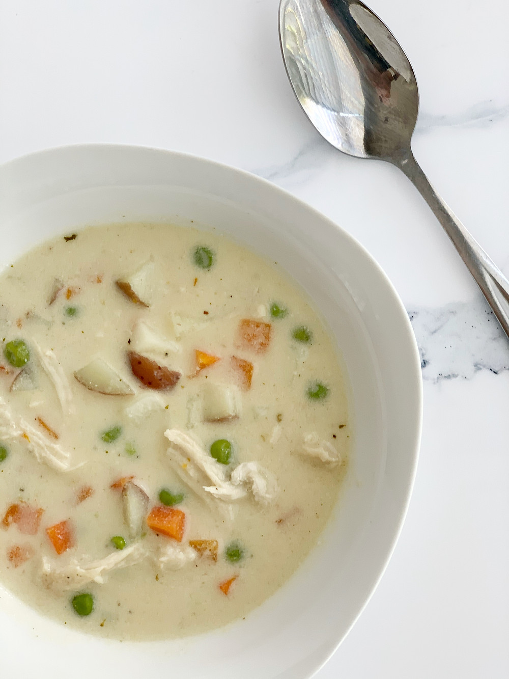 overhead shot of non-dairy chicken pot pie soup in a white bowl with a silver spoon.