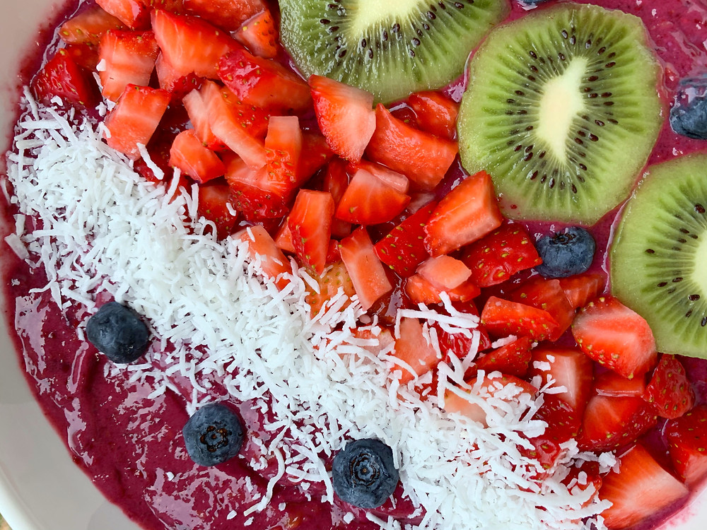 close up of blackberry smoothie bowl with blueberries, shredded coconut, chopped strawberries, and kiwi