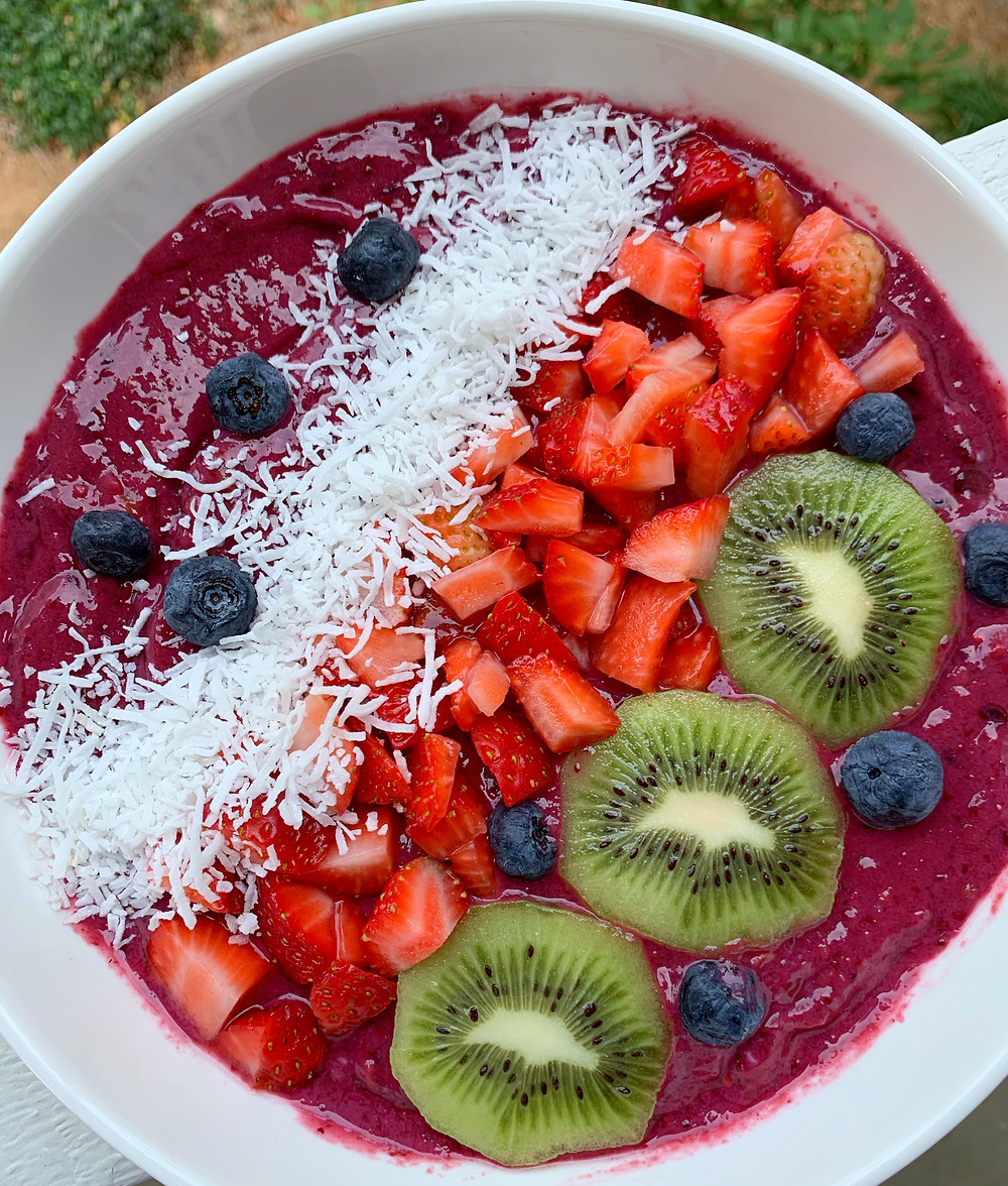 overhead shot of blackberry smoothie bowl with blueberries, shredded coconut, chopped strawberries, and kiwi