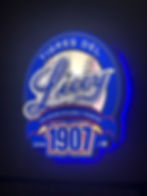 Tigres del Licey logo with baseball background, glowing blue outline. Text: "Una Historia de Gloria y Tradicion, Desde 1907."