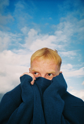 Wolf Henson with a blue sky background wearing a blue jumper pulled over his mouth
