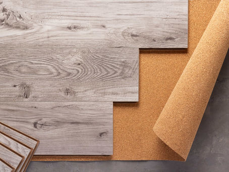 Close-up of grey wood-texture luxury vinyl planks being installed over a natural cork underlayment on a concrete subfloor. Professional flooring service in Orlando, Florida.