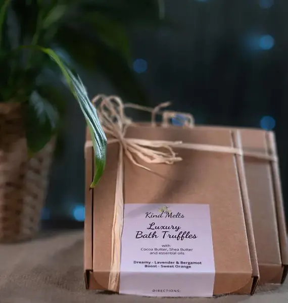 2 gift boxes sit on a natural fabric, the labels read Kind melts luxury bath truffles with cocoa butter, shea butter and essential oils.