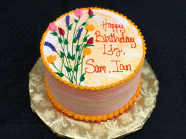 Birthday cake with flowers, "Happy Birthday Liz, Sam, Ian" on top.