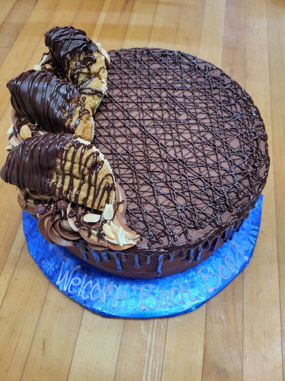 Chocolate cake "Welcome" message on blue stand with decorative chocolate toppings.