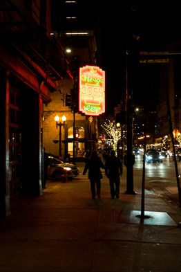 People walk at night under a bright neon sign in the city