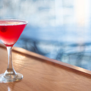 A vibrant red cocktail in a martini glass on a wooden bar closeup.