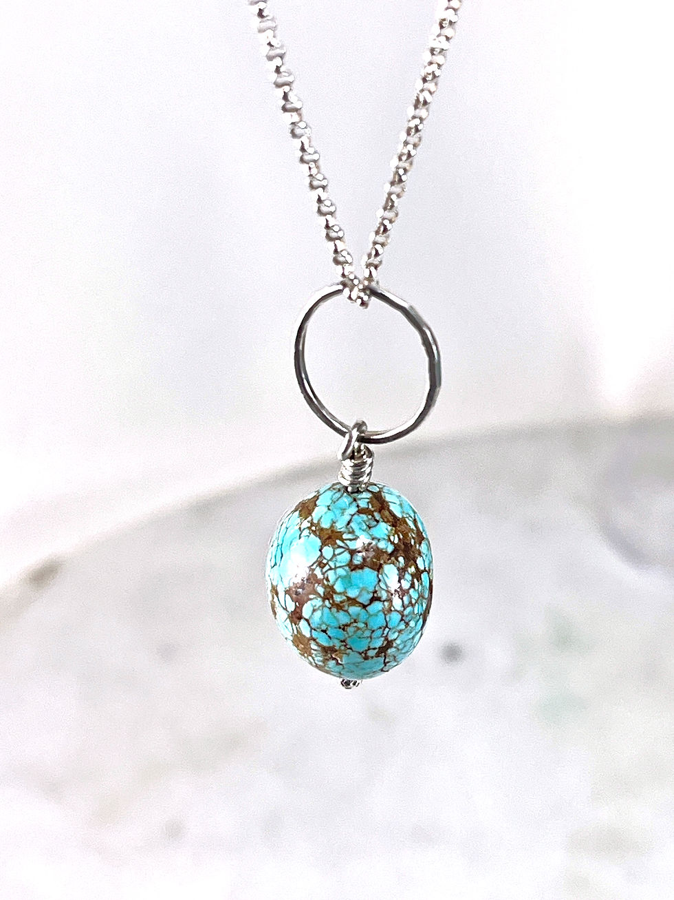 turquoise nugget on silver ring necklace hanging on white background
