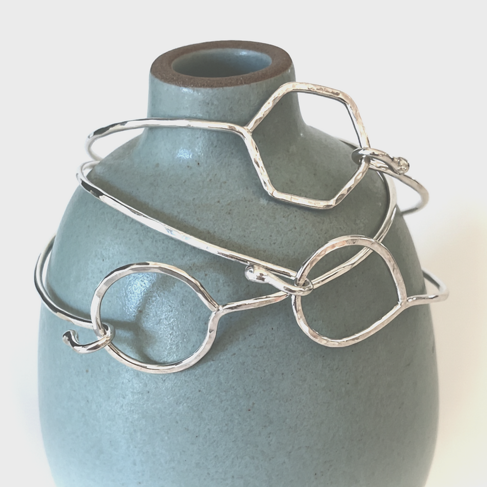 stack of silver geometric clasp bangle bracelets on a blue vase