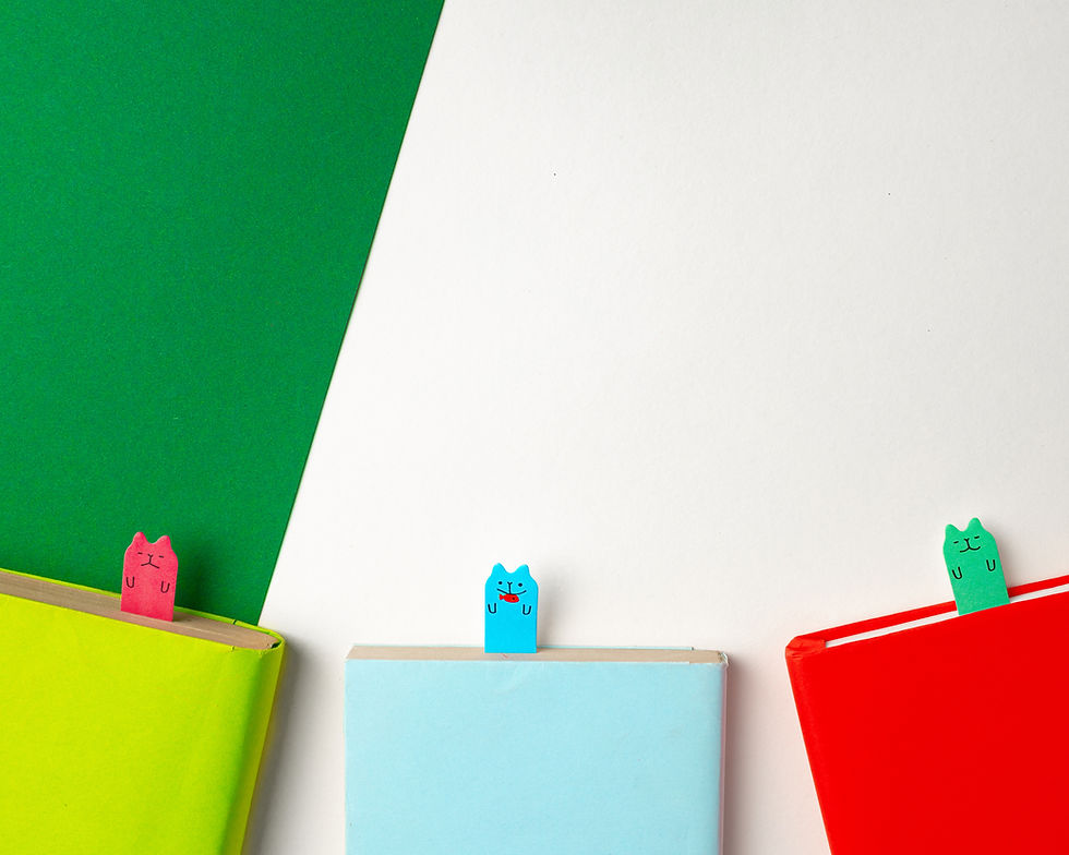 Three cut paper bookmarks with cat faces drawn on them stick out from the top of books.
