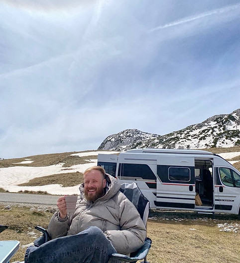 Morning coffee mug on a picnic table beside a campervan with forest backdrop