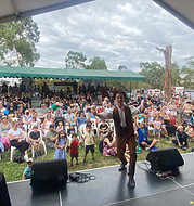 Tim Mason Magic Performing on a large stage in front of a crowd of familes watching a magic show outside on a sunny day